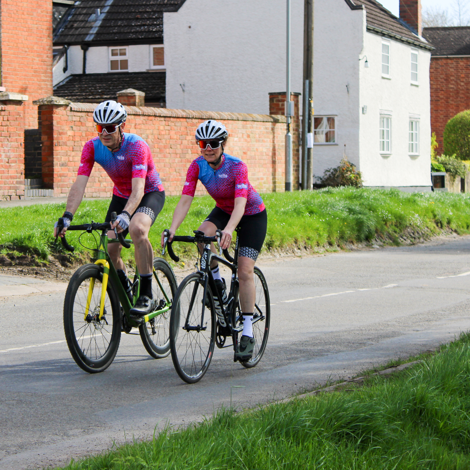 male and female cyclists riding on the road under a bridge, wearing jerseys with yellow to orange fade from left to right sleeves