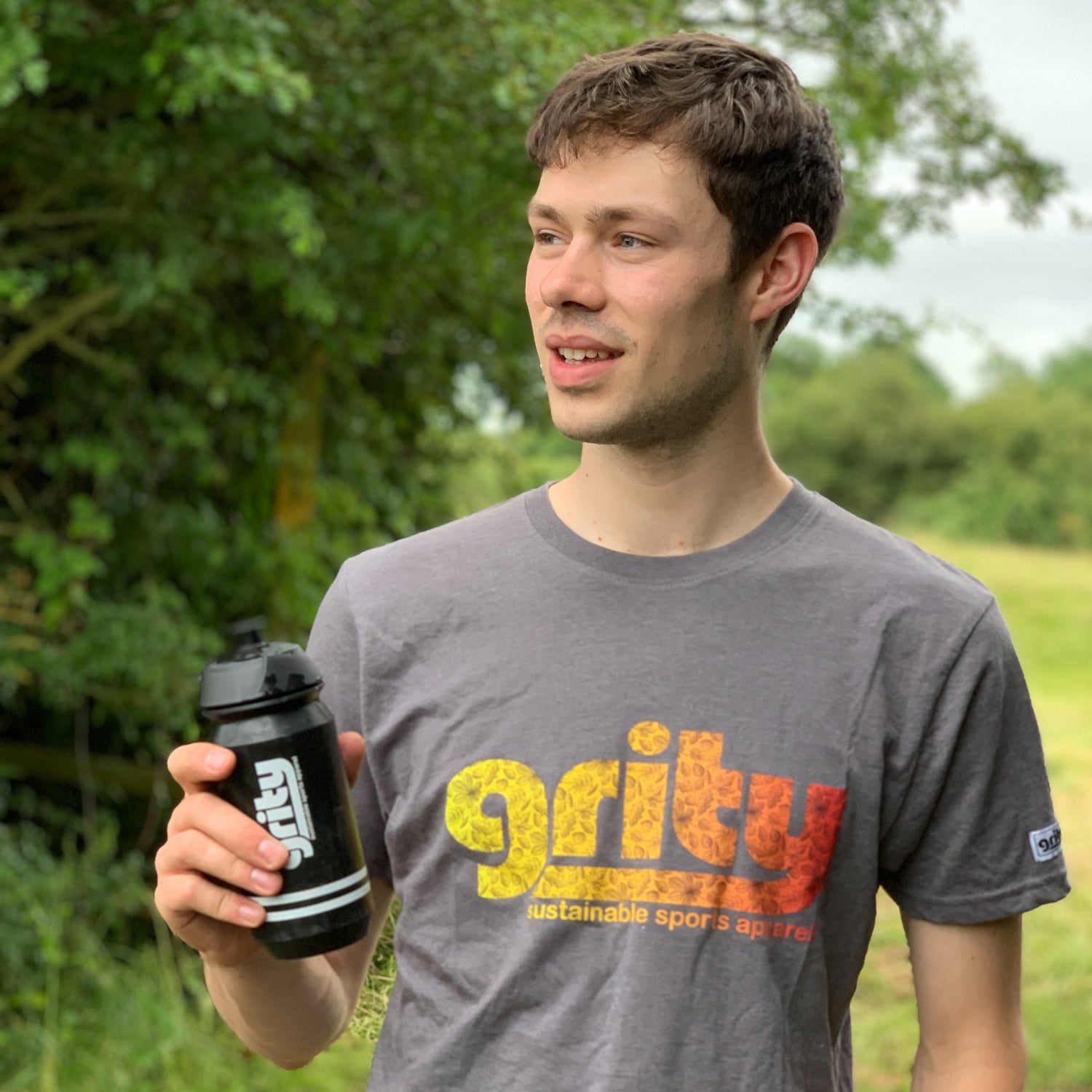 Man wearing a grey t-shirt with Grity logo in yellow fading to red, holding black grity water bottle